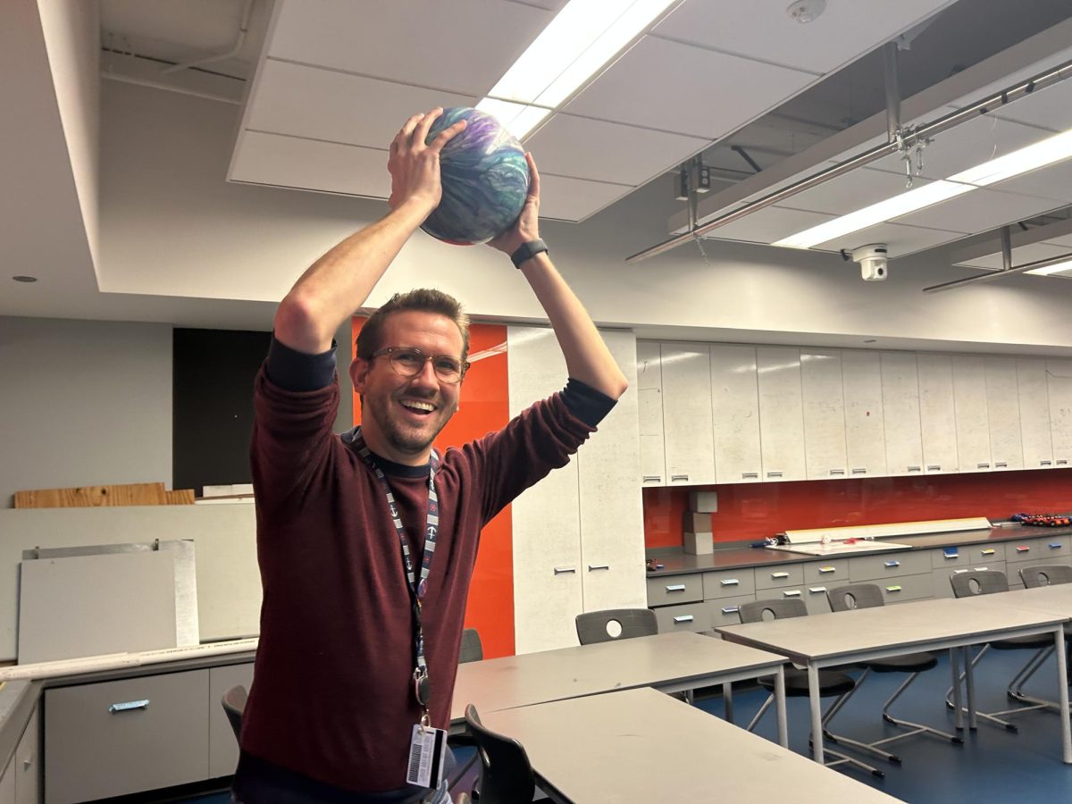 Upper School science teacher Peter Peltack holds a bowling ball above his head.