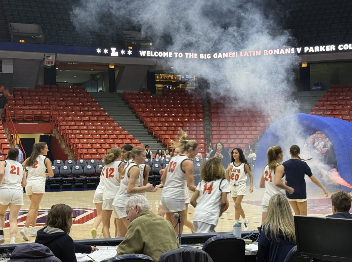 The varsity girls basketball team sprints out of a blue inflatable tunnel and onto the court.